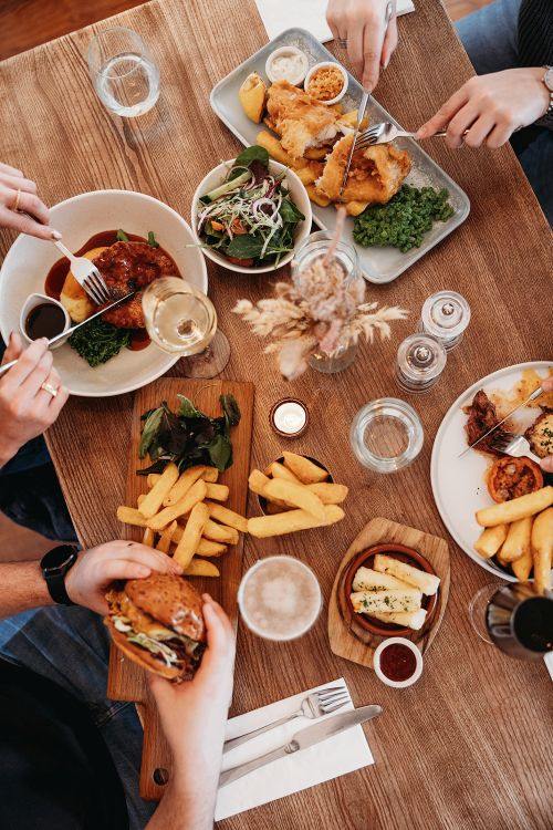 A dining table with classic pub food and drinks such as a burger, fish and chips, and homemade pie and mash.
